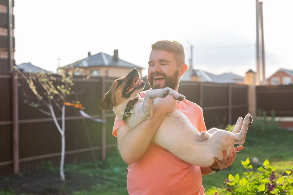 Happy man holding his happy dog in a clean yard